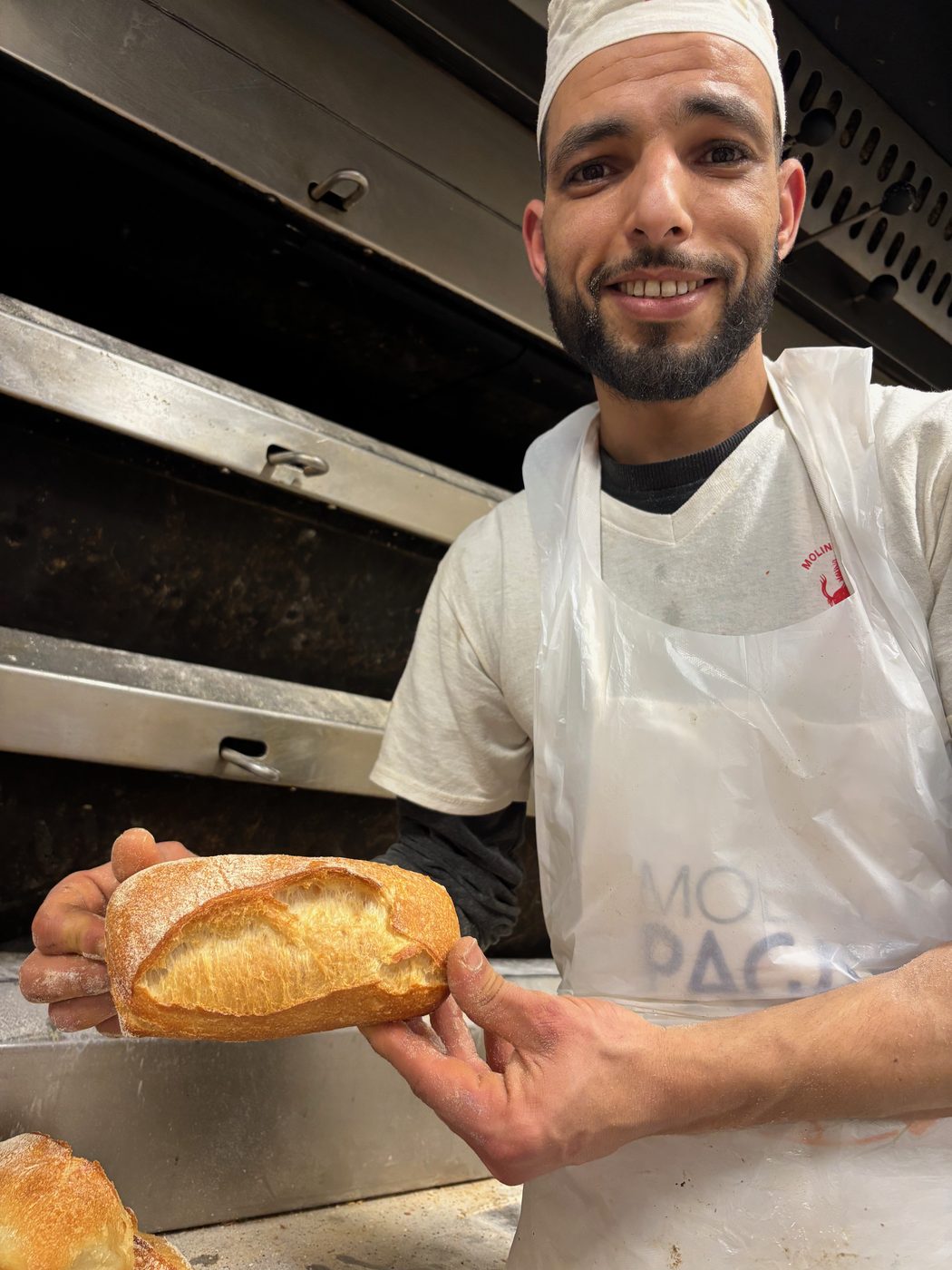 Il fornaio sorride mostrando una pagnotta appena sfornata davanti al forno