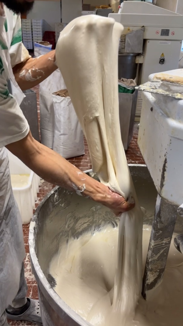 Le mani del fornaio tirano l'impasto dall'impastatrice